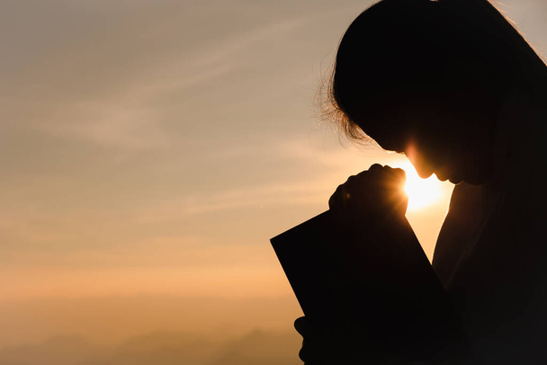 Silhouet van christelijke jonge vrouw bidden met heilige bijbel bij zonsopgang, christelijke religie concept achtergrond.  - Foto, afbeelding