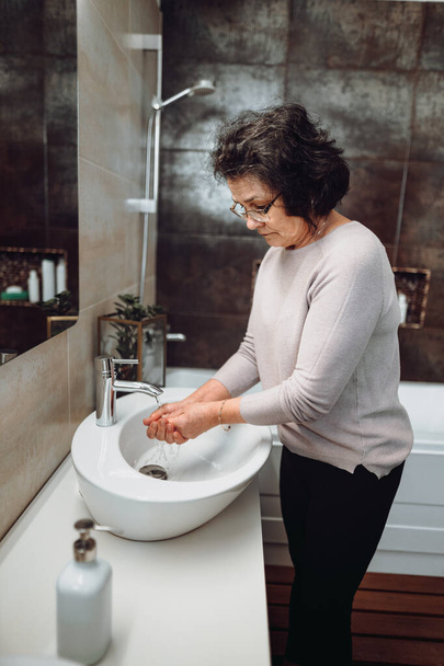 elderly woman carefully washing hands with soap and sanitiser in bathroom, details of hygiene, disinfecting hands - Фото, изображение