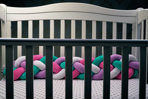 Fence in the shadow of empty children 's wooden white crib with multicolored braid, fences soft for rib. White in a dot sheet. Cozy bed for the baby. subject photo - Photo, Image