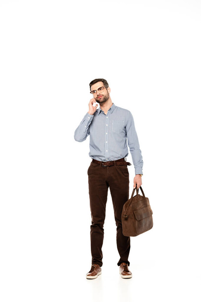 handsome and bearded businessman holding bag and talking on smartphone isolated on white   - Zdjęcie, obraz
