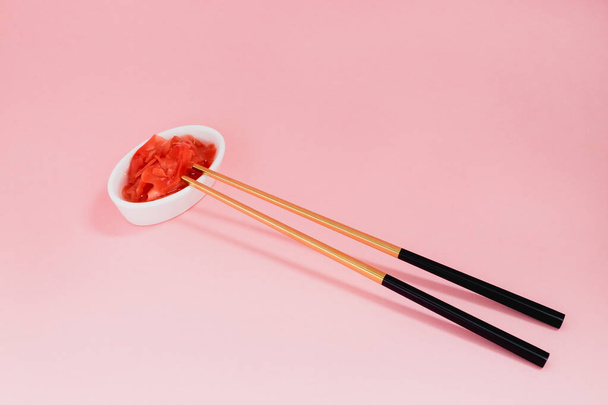 Маринованный имбирь и палочки для еды с черными ручками, сложенный крест на розовом фоне. Плоская лежала с пространством для копирования, выборочной фокусировкой. Японская еда. Горизонтальная ориентация
. - Фото, изображение