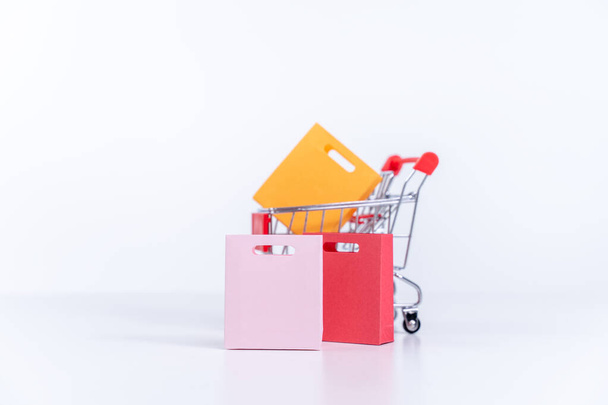Shopping bags in a silver red shopping cart isolated on white table background, concept of staying home order, close up, copy space design. - Φωτογραφία, εικόνα