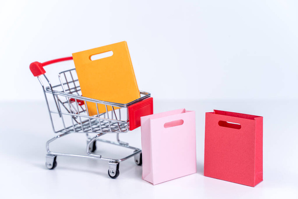 Shopping bags in a silver red shopping cart isolated on white table background, concept of staying home order, close up, copy space design. - 写真・画像
