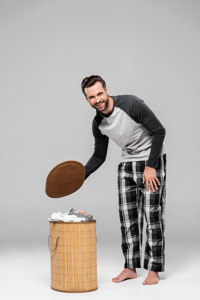 bearded man smiling while standing near laundry basket on grey  - Zdjęcie, obraz