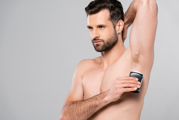 handsome and muscular man applying solid stick deodorant isolated on grey  - Фото, изображение
