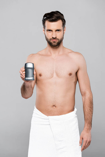 bearded and muscular man in towel holding deodorant isolated on grey  - Фото, зображення