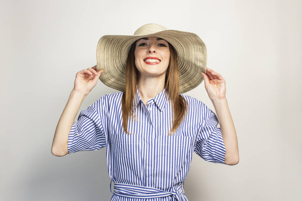 Portret młodej przyjaznej kobiety z uśmiechem w sukience i kapeluszem w szerokim rondzie na odosobnionym tle. Emocjonalna twarz. Gest zaskoczenia, radości. - Zdjęcie, obraz