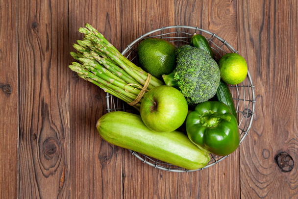 fresh natural green vegetables and fruits in a metal basket on a old wooden background. view from above - Zdjęcie, obraz