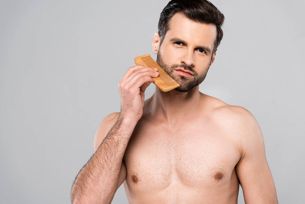 muscular man brushing beard with comb isolated on grey  - Photo, Image