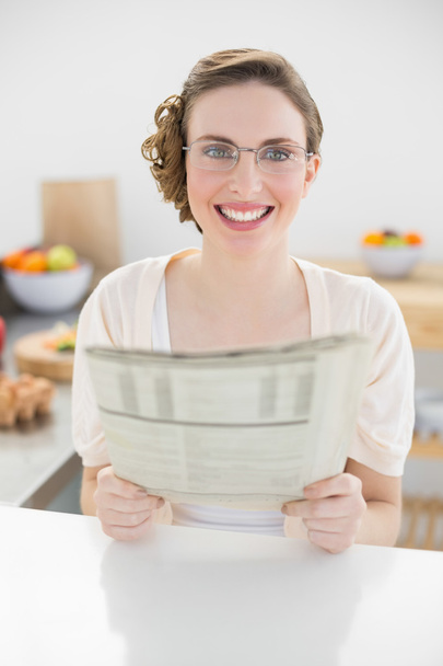 Cute woman holding newspaper sitting in her kitchen - Foto, afbeelding