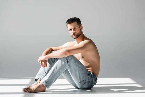 sunlight on muscular man in blue jeans sitting on grey  - Photo, Image