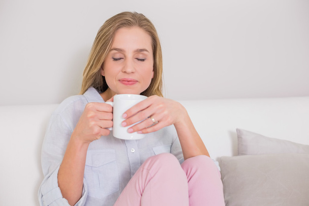 Peaceful casual blonde sitting on couch holding mug - Foto, Imagen