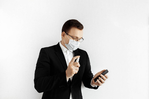 Young businessman wearing a face mask and spraying  smartphone - Fotografie, Obrázek