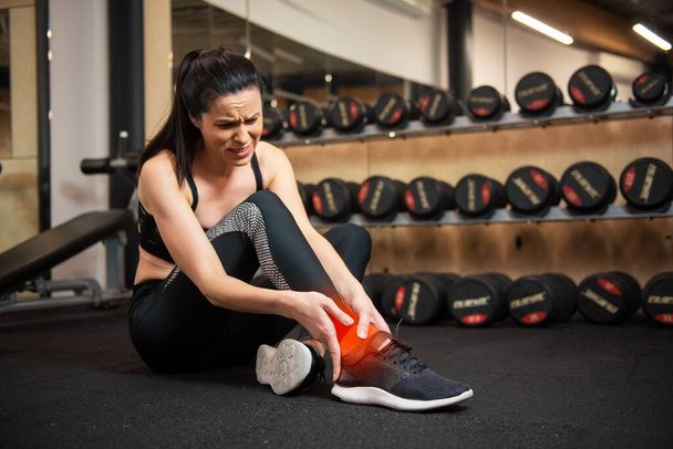 Mujer con dolor en el tobillo mientras hace ejercicio en el gimnasio
 - Foto, Imagen