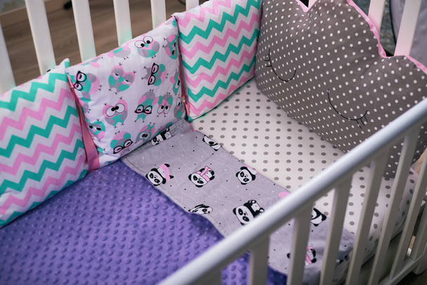 異なるパターンを持つ多色の枕は、白いシート上の子供の白い木のベビーベッドにあり、紫色の毛布で盗まれています。居心地の良い、柔らかい渇望。被写体写真 - 写真・画像