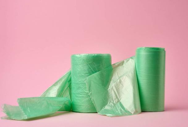 dois rolos de sacos de plástico verde para lixeira em fundo rosa, close-up
 - Foto, Imagem