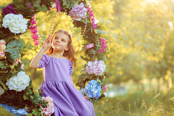 Cute little girl wearing lilac dress posing while sitting in ring decorated with flowers at the park summertime - Фото, зображення