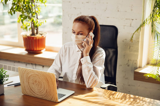 Woman working in office alone during coronavirus or COVID-19 quarantine, wearing face mask - Фото, зображення