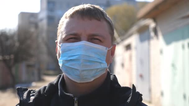 COVID-19流行中の街の通りには、顔のマスクをした男性の肖像画が立っています。ウイルスから保護マスクをした男。コロナウイルスのパンデミックからの健康と安全性の概念 - 映像、動画