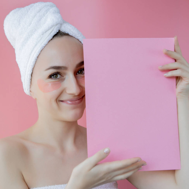 Studio shot of satisfied caucasian freckled woman wearing white towel on head, with collagen patches under eyes, standing naked against pink background. Skin care, cosmetic product concept with copy space. - Foto, imagen