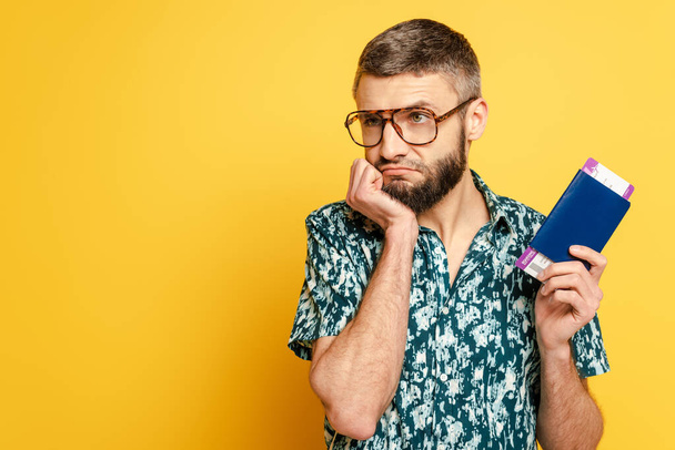 sad bearded guy in glasses with air ticket and passport on yellow - Фото, зображення