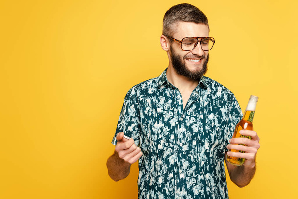 happy bearded guy in glasses with refreshing bottle of beer on yellow - 写真・画像