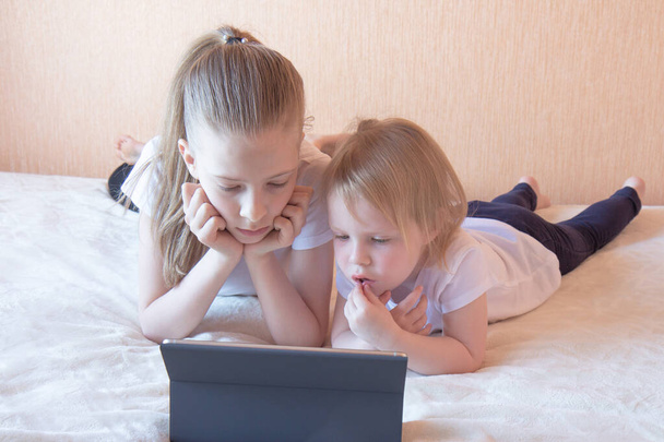Deux filles en t-shirts blancs sur le canapé avec un ordinateur portable. Enseignement à domicile. Vue latérale
 - Photo, image