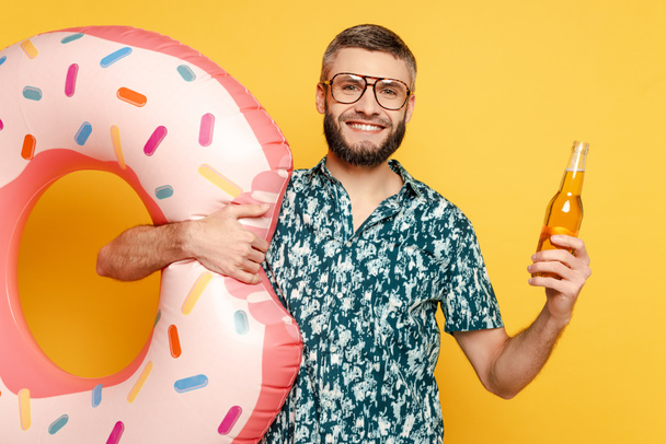 smiling bearded guy in glasses with donut swim ring and beer on yellow - 写真・画像