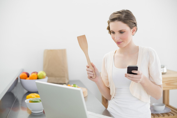 Jeune femme regardant concentré à son ordinateur portable tenant son smartphone
 - Photo, image