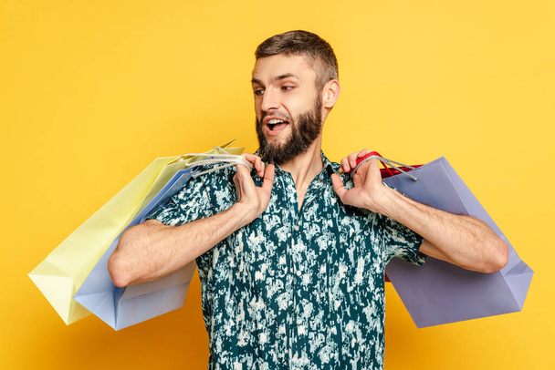 emotional bearded guy with shopping bags on yellow - Foto, imagen