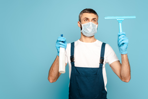 cleaner in medical mask holding detergent and squeegee on blue background - Photo, Image