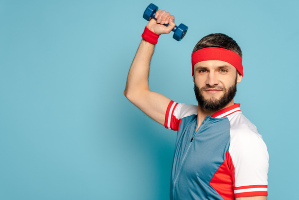 stylish sportsman exercising with dumbbell on blue background - Photo, Image