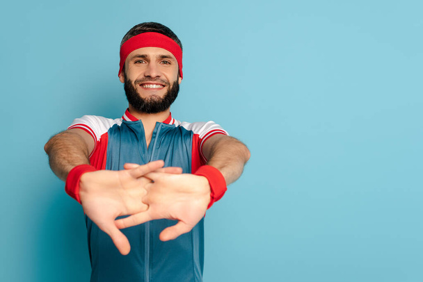 selective focus of happy stylish sportsman warming up hands on blue background - Foto, imagen