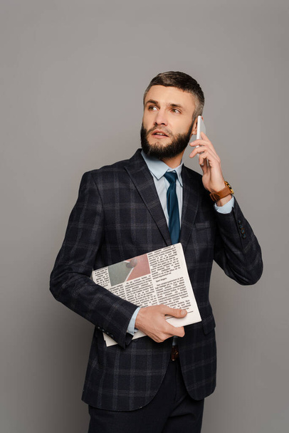 jóképű szakállas üzletember öltönyben újság beszél okostelefon szürke háttér - Fotó, kép