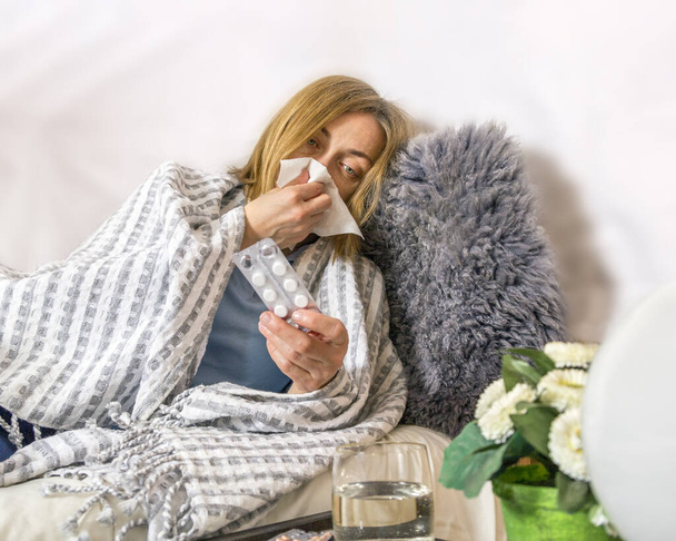 Ill sick woman lies in bed blowing her nose, coughing and drinking pills. Concept diseases of flu virus, colds, seasonal allergies, coronavirus - Fotó, kép