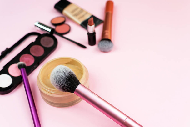 Loose face powder, brush and various cosmetic decorative makeup products on a pink background. Close up. Makeup brush and decorative cosmetics on a pastel pink background with copy space. - Foto, Imagem