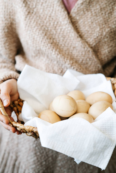 niña en un cárdigan de punto de color polvoriento sostiene una cesta de mimbre natural con huevos de Pascua pintados en un tono pastel de moda con grietas en la concha.
 - Foto, Imagen