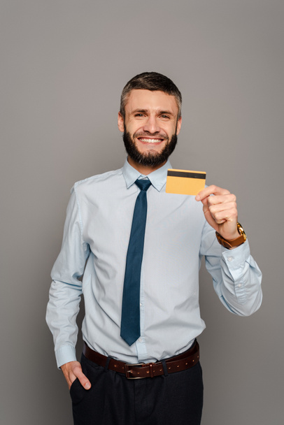 smiling handsome bearded businessman with credit card on grey background - Photo, Image