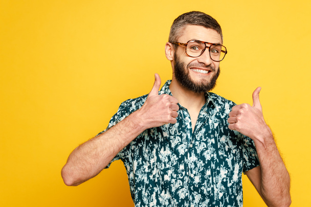 sonriente barbudo chico en gafas mostrando los pulgares hacia arriba en amarillo
 - Foto, Imagen