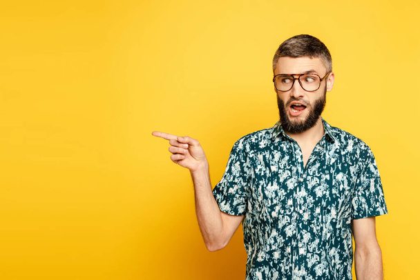 bärtiger Typ mit Brille zeigt mit dem Finger zur Seite auf gelb - Foto, Bild