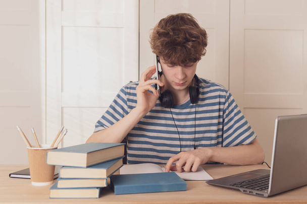 Teenager talking on a cell phone, learning using a laptop.A thoughtful kid at his desk is thinking about learning.Distance learning because of the epidemic coronavirus - Фото, зображення