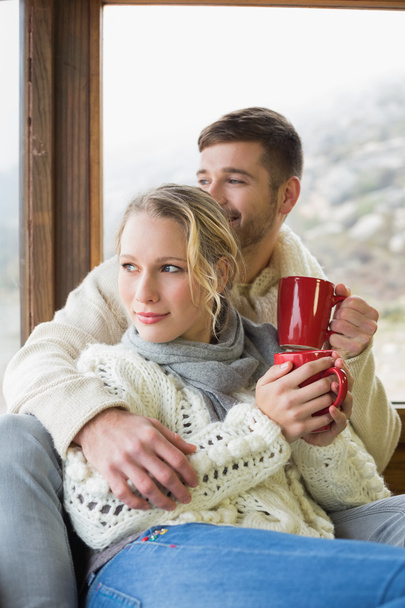 Couple in winter wear with cups looking out through window - Фото, зображення