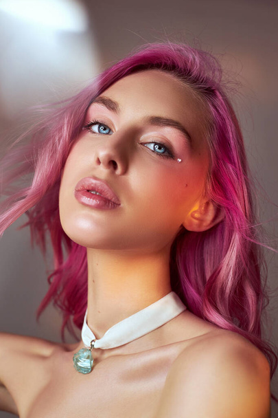 Art beauty portrait of a woman with pink hair, creative coloring. Bright colored highlights and shadows on the face, a girl with jewelry. Dyed hair in the wind - Фото, изображение