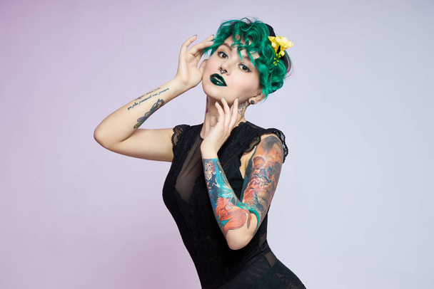 Woman with creative green coloring hair and makeup, toxic strands of hair. Bright color curly hair on the girl head, professional makeup. Woman with tattoo - Photo, image