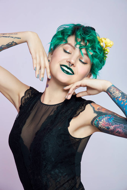 Woman with creative green coloring hair and makeup, toxic strands of hair. Bright color curly hair on the girl head, professional makeup. Woman with tattoo - Foto, Imagem