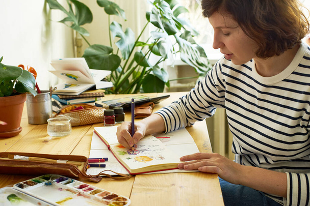 Close-up image of artist drawing in a sketchbook. Female designer working from home. Creative cozy workplace - Fotó, kép
