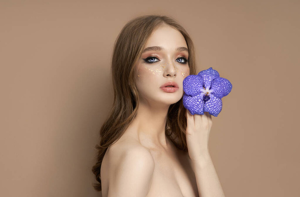 Beauty portrait of a woman with a blue Vanda Orchid in her hand. Natural cosmetics made of flower petals, clean delicate skin of the girl face - Φωτογραφία, εικόνα