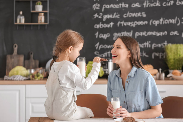 Mutter mit ihrer kleinen Tochter trinkt Milch mit Keksen in der Küche - Foto, Bild