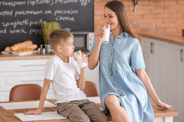Mother with her little son drinking milk in kitchen - 写真・画像