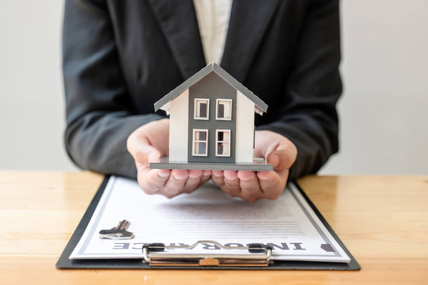 Dłoń agenta ubezpieczeniowego domu posiada model domu, aby chronić bezpieczeństwo klientów kupujących. - Zdjęcie, obraz